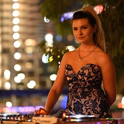 A woman in a dress stands beside a DJ mixer at Elizabeth Quay food event.