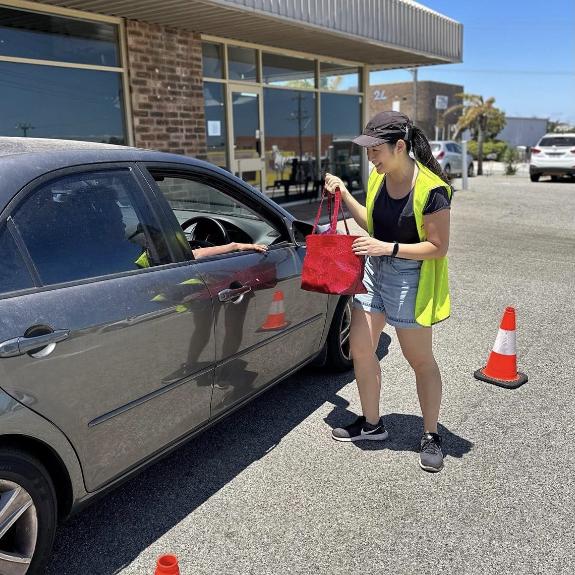 A woman in a yellow vest stands beside a car at Elizabeth Quay food.